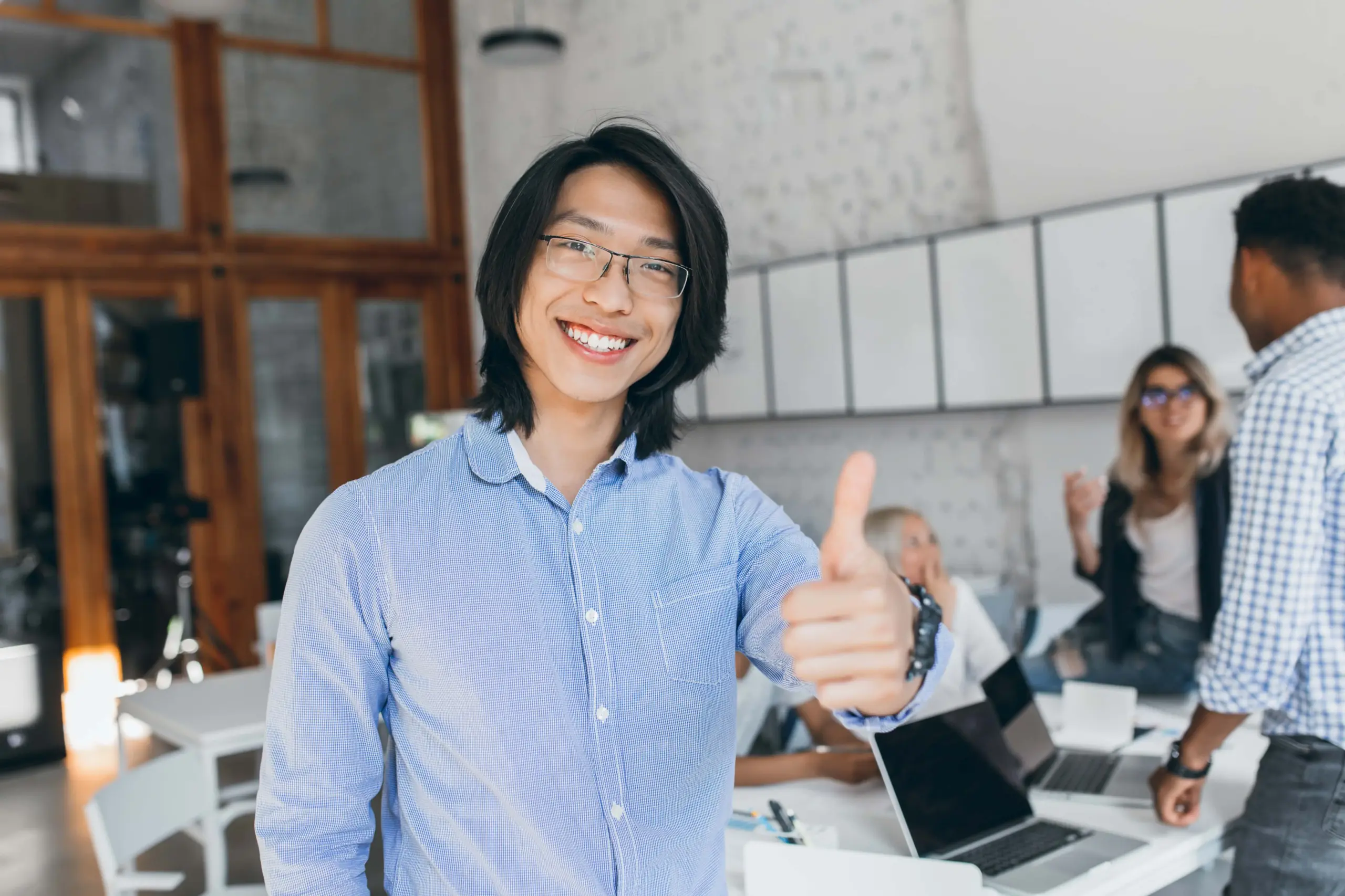 asian laughing boy posing with thumb up beginning workday chinese office worker blue shirt glasses smiling with laptop (2)