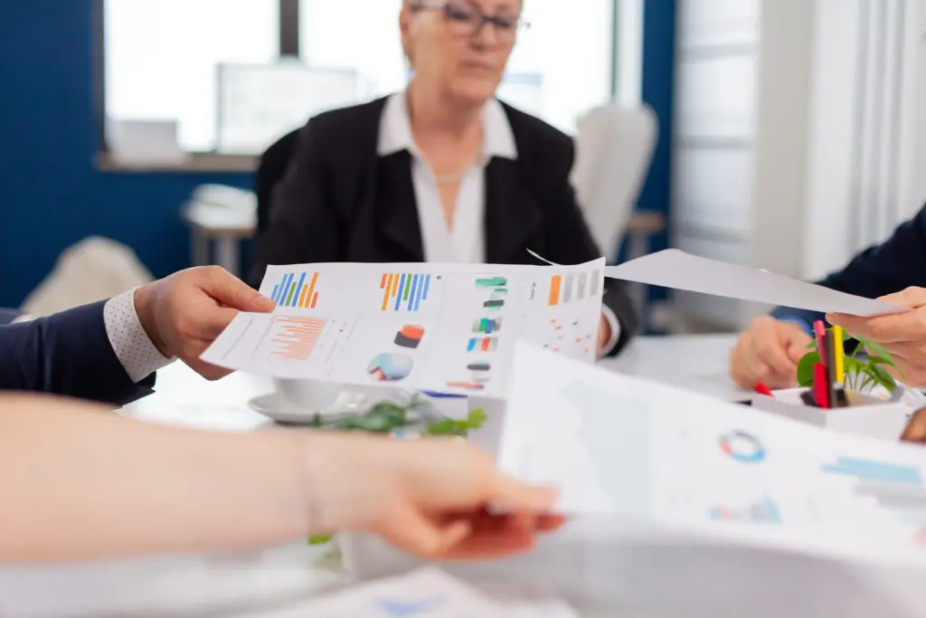 confident company manager giving working tasks diverse teamworkers analysing paperwork with graphs sitting start up office (1)